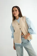 Chaleco de tejido de punto en color beige, con escote en V, cierre frontal con botones oscuros y dos bolsillos delanteros aplicados.