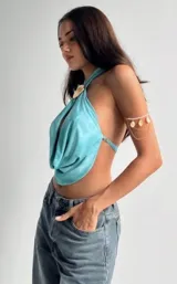 Top halter celeste con abertura en el centro y detalle de aplique con forma de concha dorada en el cuello.