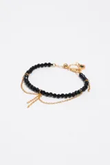 Pulsera de cuentas de cristal facetado negro combinada con finas cadenas doradas colgantes y dije con detalles esmaltados.
