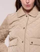 Campera corta capitoneada Michael Kors de color beige, con diseño acolchado en rombos, cuello camisero, cierre frontal de botones metálicos a presión y bolsillos frontales con solapa. Incluye un pequeño bolsillo en la manga.