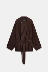 Chaqueta marrón oscuro con cuello solapa, manga larga ancha con trabilla y botón, y cinturón del mismo tejido anudado a la cintura. Cierre frontal cruzado con un botón visible.