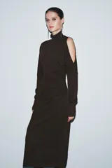 Vestido midi de punto color marrón, con cuello subido, manga larga y diseño cut out en un hombro. Presenta frunces laterales en la cintura que aportan un efecto drapeado.