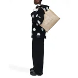 Bolso tote de lona en color beige, con diseño rectangular y estructura rígida. Presenta el nombre del modelo y la marca estampados en la parte frontal en color blanco. Cuenta con doble asa superior, cierre de cremallera en la parte superior y compartimento principal amplio.