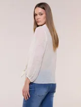 Blusa confeccionada en gasa semitransparente con sutil acabado plisado y estampado floral en tonos suaves. Presenta cuello solapa redondeado, escote en V y botonadura frontal. Mangas largas con puños elásticos y ruedo anudado en la parte inferior frontal.