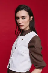 Chaleco blanco de denim con diseño cruzado asimétrico y cierre frontal con tres botones carey.
