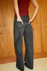 Jeans de tiro alto, color gris oscuro lavado, con pierna ancha extra larga (full length) y diseño de cintura cruzada asimétrica con cierre frontal de cremallera y botones metálicos.