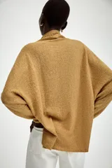 Jersey de punto con textura, color crudo, de cuello subido y manga larga. Presenta un diseño holgado con bajo asimétrico y aberturas laterales.