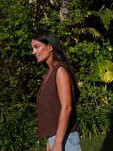 Chaleco de lino en color beige, con escote en V, cierre frontal con botones y bolsillos delanteros decorativos.