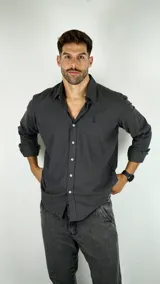 Camisa de manga larga en color gris oscuro, con cuello clásico y cierre frontal de botones. Presenta un pequeño logo bordado en el pecho.