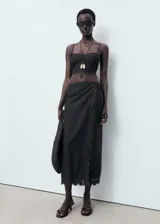 Falda midi recta de color negro, confeccionada en algodón con detalles bordados en el borde y cierre de cremallera lateral.