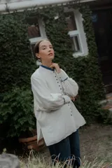 Camisa de corte oversize color crudo, con cuello mao y puños con detalle de volados en color azul. Presenta cierre frontal con botones forrados y mangas largas abullonadas.