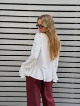 Blusa blanca de textura arrugada, con escote en V y lazos para anudar. Presenta mangas largas con puños acampanados y un diseño con volado en el ruedo.