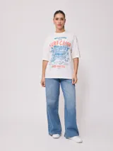 Remera blanca de algodón con estampado frontal de estilo playero con texto en color coral y azul.