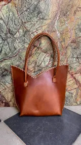 Cartera de cuero mediana con manijas largas, diseño con borde superior en corte en V y terminación artesanal con costuras contrastantes.