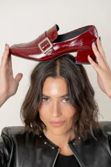 Mocasin de cuero charolado color bordó, con punta cuadrada, taco bloque bajo y detalle de tira con hebilla metálica plateada en el empeine.