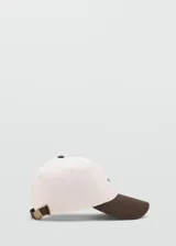 Gorro tipo gorra con visera, confeccionado en algodón, con diseño bicolor en color crudo y marrón, cierre regulable con hebilla metálica y detalle de mensaje bordado.