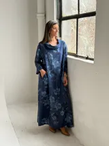 Vestido largo de lino azul marino con estampado floral en tonos más claros, de corte amplio, con cuello tipo cowl y mangas largas.