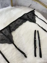 Conjunto de lencería compuesto por bralette triangular, tanga y portaligas, confeccionado íntegramente en encaje negro con detalles de breteles regulables.