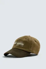 Gorra de seis paneles confeccionada en tejido de algodón con visera de efecto ante en contraste. Presenta un bordado frontal con el texto 'Freedom in every stiff born since 1934' y ajuste regulable en la parte posterior.