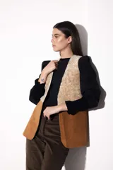 Chaleco marrón de cuero vacuno con aplique de corderito color crema. De corte recto con aberturas inferiores en los laterales y adelante.