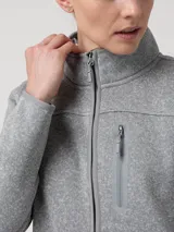 Polar de mujer color gris claro, con cierre frontal completo y cuello alto. Presenta un bolsillo vertical con cierre en el pecho y bolsillos laterales con cierre.