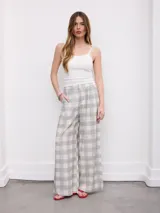 Pantalón de corte ancho y fluido, con estampado a cuadros en tonos grises y blancos, cintura alta con trabillas y bolsillos laterales.