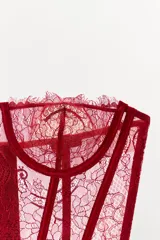 Corsé sin mangas color rojo oscuro, confeccionado en encaje con patrón floral. Presenta aros para soporte, escote recto y varillas visibles que estilizan la figura. El borde inferior tiene un acabado festoneado con flecos.