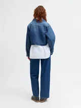 Sobrecamisa cropped de denim azul medio, con cuello clásico, mangas largas globo y dos bolsillos de parche con tapa en el pecho.