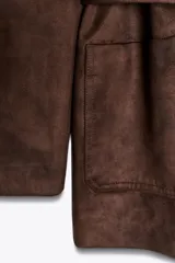 Chaqueta marrón de efecto ante con cuello solapa, manga larga, bolsillos delanteros de plastrón, cierre frontal con botones y cinturón a juego.