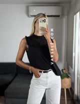 Blusa blanca sin mangas, de símil lino, con cuello alto y detalle de encaje calado y volados en el escote.