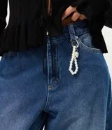 Pantalón baggy de jean azul con tiro medio, corte holgado, recortes en las rodillas y llavero decorativo con perlas y dije de corazón.