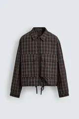 Cazadora de corte cropped confeccionada en algodón con estampado de cuadros. Presenta cuello solapa, cierre frontal con cremallera, mangas largas con puños abotonados y bolsillos frontales de plastrón. El bajo es ajustable mediante cordón.