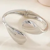 Pulsera rígida plateada con cierre de bisagra y terminaciones en forma de gota.