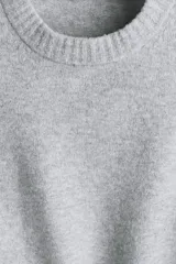 Buzo de punto gris melange con acabado cepillado, cuello redondo, mangas largas y puños y bajo acanalados.