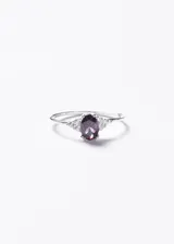 Anillo de plata 925 con piedra central de zirconia en corte oval color violeta, flanqueada por pequeñas piedras de zirconia transparentes a cada lado.