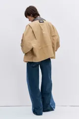 Cazadora de corte oversize en color beige, con cuello de solapa en contraste de color oscuro, cierre frontal con botones y bolsillos laterales.