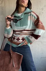 Sweater de tejido de punto con diseño a rayas horizontales y patrón geométrico en tonos verde, marrón y beige. Presenta cuello alto con cierre frontal, mangas largas abullonadas con puños ajustados y corte holgado.