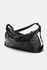 Bolso tipo saca color negro, de diseño flexible y acabado con efecto gastado. Cuenta con un asa ajustable para el hombro, detalles de hebillas y herrajes metálicos laterales, además de un cierre superior de cremallera metálica.