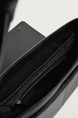Bandolera de diseño rectangular en color negro con acabado texturizado. Cuenta con una solapa frontal con detalle metálico, cierre imantado y asa de hombro ajustable. El interior incluye un bolsillo plano y otro con cierre, además de un bolsillo plano adicional en la parte frontal.