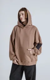Hoodie oversize color marrón, confeccionado en algodón rústico. Presenta capucha forrada, bolsillo frontal tipo canguro y un bolsillo utilitario con cierre en la manga izquierda, con detalles en microfibra.