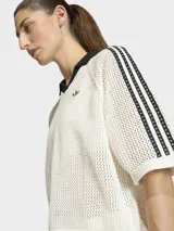 Polo de crochet color blanco con cuello polo negro en V, mangas cortas con las icónicas tres tiras de Adidas en negro y logo de la marca bordado en el pecho.