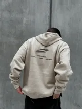 Canguro beige con capucha ajustable con cordones, bolsillo tipo canguro y estampado con diseño abstracto en negro.