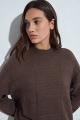 Sweater de punto gris con cuello a la base y diseño de trama geométrica en relieve. Presenta un calce relajado con mangas largas y puños tejidos.
