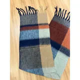 Bufanda rectangular de tejido grueso con diseño de cuadros en tonos azul, naranja, gris y beige, terminada con flecos en los extremos.