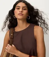 Blusa sin mangas color marrón, con escote redondo y corte recto. Presenta paneles laterales en tejido texturizado con rayas y una abertura vertical en la espalda con cierre discreto.