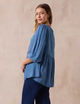 Blusa celeste de tencel y rayón, marca Marissa Olivia. Tiene cuello redondo, escote en V con aplique de crochet y lazo de ajuste. Corte en cintura y espalda. Manga larga amplia con puño elastizado.