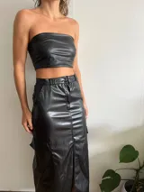 Falda midi de cuero sintético color negro, con corte recto, abertura frontal, bolsillos cargo laterales y cierre con botón y cremallera.