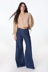 Pantalón de pierna ancha con acabado brillante, confeccionado en lino. Presenta un diseño de tiro medio con cierre de botón y cremallera, bolsillos traseros y etiqueta de marca en la cintura.