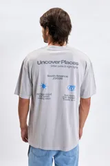Remera de manga corta en color gris melange con efecto lavado. Presenta una estampa gráfica en la espalda con el texto 'Uncover Places' y detalles tipográficos en tonos gris oscuro y azul.