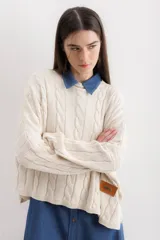 Sweater de punto con diseño de trenzas verticales, cuello redondo y corte holgado. Presenta una etiqueta de cuero sintético con el logo de la marca en la parte inferior.